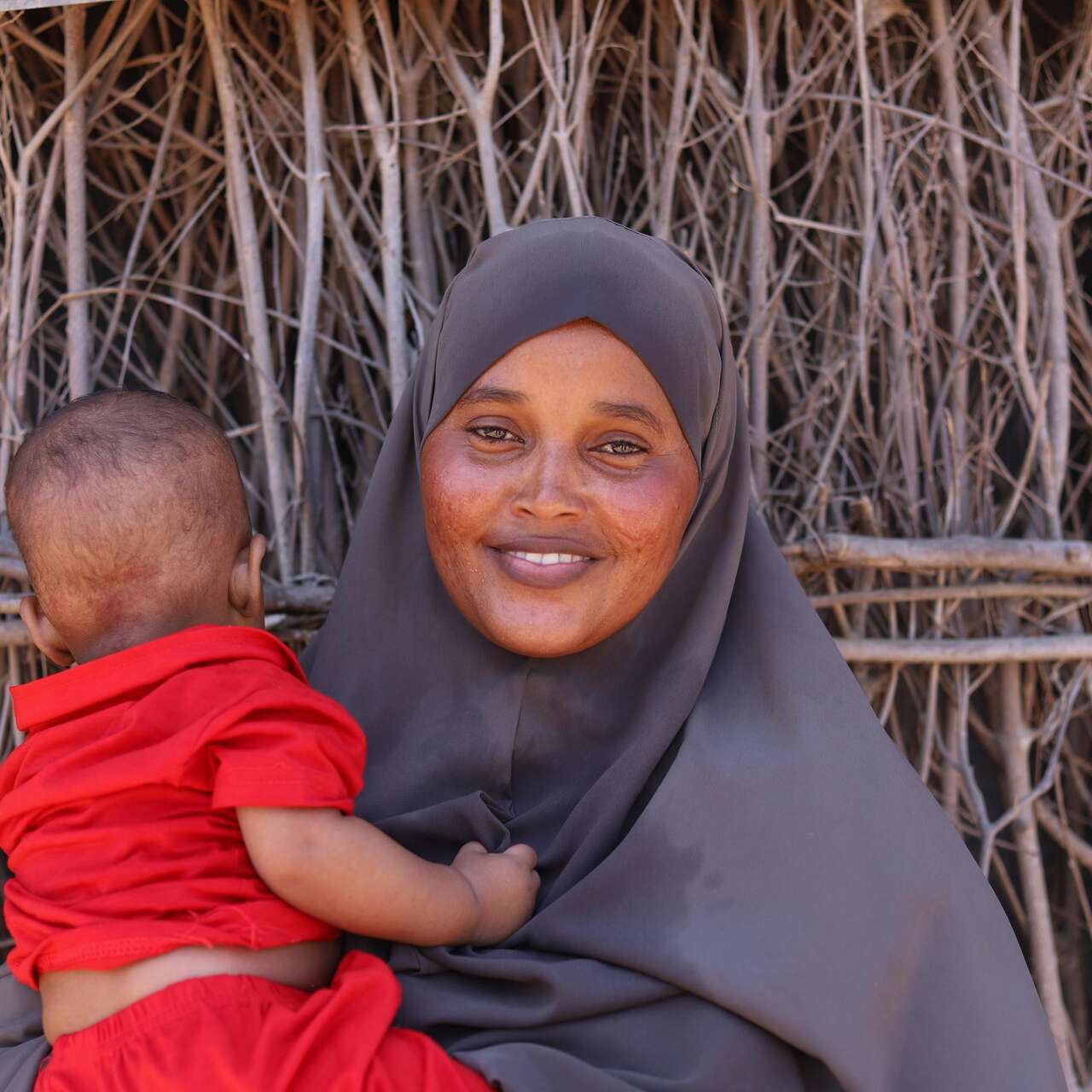24 January 2024, Dadaab Refugee Camp, Kenya. Fatuma, who is 25 years old, stands outside her home with her son.
